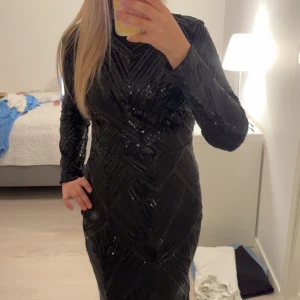 Svart glittrig långklänning - Säljer en svart långklänning med glittriga paljetter och snyggt mönster. Klänningen har lång ärm och figurnära passform som ger en riktigt elegant look. Perfekt för dig som vill sticka ut och glänsa på nästa stora tillställning!