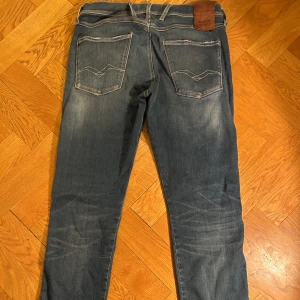 Blå jeans från Replay med slitningar - Säljer ett par blå hyperflex jeans från Replay med slitningar och ett lappat hål på benet vilken såklart sänker priset. Klassisk femficksmodell med raka ben och snygga detaljer på bakfickorna. Jeansen har slim passform och är tillverkade i mjukt denimtyg. De är väldigt bekväma och stretchiga men samtidigt stilrena