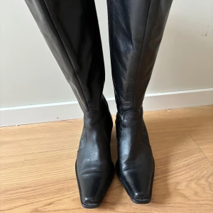 Svarta stövlar i skinn - Höga svarta stövlar, tillverkade i äkta skinn från Italien. Använda ett fåtal gånger på grund av att de är för små De har spetsig tå, blockklack och dragkedja på insidan. Klassisk modell med högt skaft med resår. 