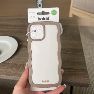 Holdit Wavy Case för iPhone 12/12 Pro - Snyggt och trendigt mobilskal från Holdit, designat för iPhone 12/12 Pro. Tillverkat av 100% återvunnet material, slitstarkt och stötdämpande (2m). Greppvänlig, stödjer trådlös laddning inkl. MagSafe. Oöppnad förpackning, nyskick utan synliga defekter.