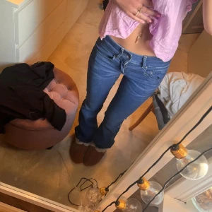 Blå bootcut jeans låg midja - Säljer ett par blå jeans med bootcut-modell och låg midja. Jeansen har klassisk femficksdesign och är tillverkade i denim. Insidan av benen har ett coolt mönster i ljusare blått när man viker upp dem. Perfekta för dig som gillar en avslappnad och trendig stil.