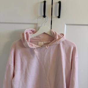 Ljusrosa hoodie från Gina Tricot - Säljer en ljusrosa hoodie från Gina Tricot med huva och snörning. Tröjan har lång ärm och är tillverkad i mjuk bomullsmix, perfekt för chill dagar. Enkel design utan mönster eller tryck, passar dig som gillar stilrena plagg.