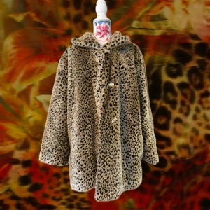 Leopardmönstrad pälsjacka med huva - Säljer en fluffig och oversized pälsjacka med leopardmönster. Jackan har huva, stora knappar framtill och långärmad design. Färgen är beige med svarta och bruna detaljer. Perfekt för dig som vill sticka ut och hålla dig varm under höst och vinter.