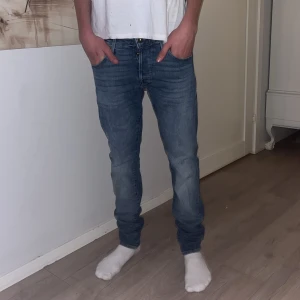 Jack & Jones blåa jeans - Snygga blå jeans från Slim Glenn i storlek 29/32 Från Jack Jones . Modellen har en slim passform med klassisk femficksdesign och guldfärgade sömmar. Jeansen är tillverkade i mjukt denimtyg och har en normal midja. Perfekt för dig som gillar en smal siluett. Modellen är 182. 