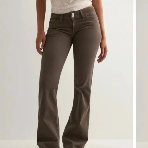 Bruna bootcut jeans från Nelly - Helt nya. Ligger kvar i förpackning. Snygga bruna bootcut jeans från Nelly med hög midja och klassisk femficksdesign. Jeansen har dekorativa sömmar på bakfickorna och två knappar framtill. Materialet är mjukt och stretchigt för en bekväm passform. 