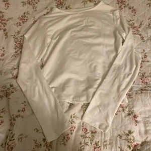 Vit långärmad topp i polyester, S - En stilren vit långärmad topp i storlek S, tillverkad av mjuk och stretchig polyester med lite spandex för extra komfort. Enkel design med rund halsringning och raka ärmar, perfekt att matcha med jeans eller kjol.Basic-okänt märke,nyskick 