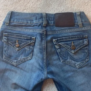 Blå jeans från LTB - Snygga blå jeans från Ltb med låg midja.  Jeansen har coola detaljer på bakfickorna med broderad våg och knappar, samt klassisk femficksdesign. Materialet är jeans med lätt tvättad look och slitningar för en trendig vibe. På dessa bilder får jag inte med hela byxorna, så skriv såklart till mig ifall du har några frågor eller funderingar!!💕Stolek på byxorna är W25 L30. 