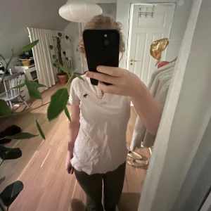 Ljus rosa piké från Abercrombie & Fitch - En ljus rosa pikétröja från Abercrombie & Fitch med stretch och knappar framtill. På bröstet finns en svart broderad älg. Skön bomullskvalitet och korta ärmar, perfekt för en chill och clean look. Det står på tröjan att den är L men själv är jag S då den sitter bra på mig💕