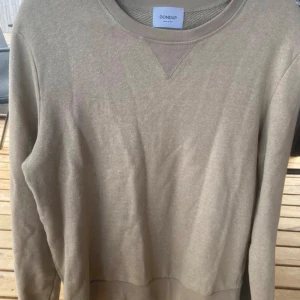 Beige sweatshirt från Dondup - Säljer en stilren beige sweatshirt från Dondup, tillverkad i Italien. Tröjan har rund halsringning, ribbade muddar och en diskret detalj i nacken. Perfekt för dig som gillar enkel och clean stil.