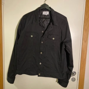 Svart jacka  från Weekday large  - Svart jacka  från Weekday med klassisk krage och silverfärgade knappar framtill. Jackan har två bröstfickor med lock och knapp, samt långa ärmar. Perfekt för dig som gillar enkel och stilren design.