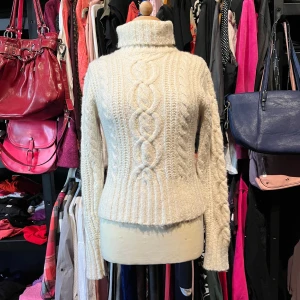 Vit polotröja med flätstickning - Säljer en mysig vit polotröja med snygg flätstickning framtill, baktill  och på ärmarna. Tröjan har hög krage och är ribbstickad i nederkant och vid ärmslut. Materialmix av ull, bomull och akryl gör den både varm och lmjuk. Perfekt för kyliga dagar!