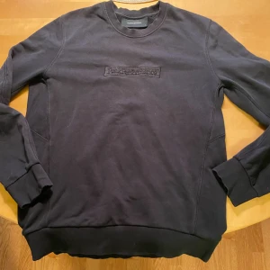 Svart sweatshirt från Peak Performance - Svart sweatshirt från Peak Performance med broderad logga på bröstet. Klassisk rund halsringning, ribbade muddar och mjukt material. Perfekt för en chill och stilren look.