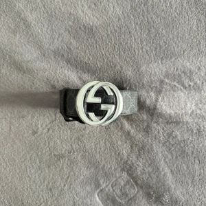 Gucci bälte  - Säljer ett svart Gucci bälte med klassiskt GG-mönster och en stor, rund silverfärgad GG-spänne. Bältet är gjort av äkta skinn och har en snygg, stilren look som lyfter vilken outfit som helst. Perfekt för dig som gillar exklusiva accessoarer och vill sticka ut.