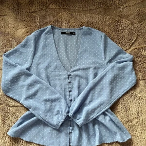 Blå prickig blus från Bik Bok XS - Supersöt ljusblå blus från Bik Bok i storlek XS. Blusen har ett prickigt mönster, v-ringning och knappar framtill. Långa ärmar med lätt puff och en volang nedtill ger en feminin look. Perfekt att styla med jeans eller kjol för en chill vibe. 