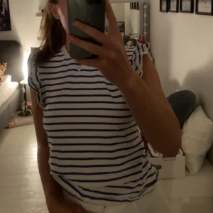 Randig vit och blå t-shirt - Säljer en fräsch vit t-shirt med blåa horisontella ränder. T-shirten har korta ärmar med lätt volangkant och rund halsringning. Perfekt för dig som gillar en enkel men snygg stil. Materialet känns mjukt och bekvämt mot huden. Lite Stockholmsstil oklart märke men gissar på Shein 