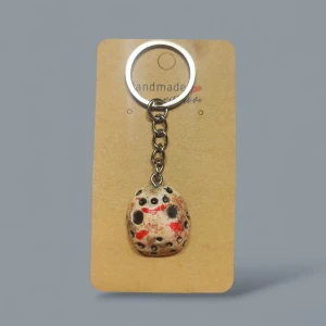 Nyckelring Jason mask - Unik nyckelring med en handgjord Jason mask, inspirerad av skräckfilm. Masken är beige med svarta prickar och röda detaljer, fäst i en silverfärgad kedja och ring. Perfekt för dig som gillar coola och annorlunda accessoarer.