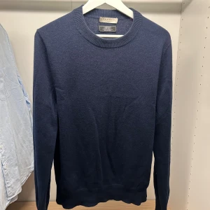 Sandro Kashmirtröja Navy - Snygg mörkblå tröja från Sandro i 100% kashmir. Klassisk rund hals och ribbade muddar vid ärmslut och nederkant. Långärmad och mjuk, perfekt för dig som gillar stilrena och lyxiga plagg. (Ett litet hål vid ena ärmen)