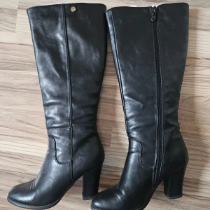 Svarta stövlar med klack, storlek 36 - Säljer ett par svarta stövlar i skinnimitation med hög klack och rund tå. Stövlarna har dragkedja på insidan och en stilren, klassisk look som passar till många outfits. Snygga till både jeans och kjol, perfekta för höst och vinter. Inköpta I Italien . 