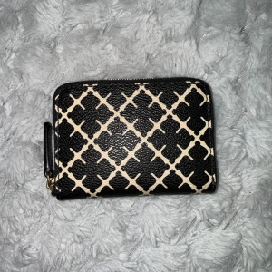 Svart och beige plånbok från Malene Birger  - Snygg plånbok från Malene Birger i svart och beige med rutigt mönster. Plånboken har dragkedja runtom och insida i beige tyg. Perfekt storlek för kort och mynt, och lätt att ta med i väskan. Jättefint skick, märks knappt att den är använd! 