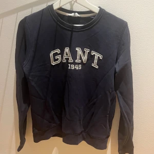 Mörkblå sweatshirt från GANT - Säljer en mörkblå sweatshirt från GANT med broderad logga och årtal 1949 på bröstet. Tröjan har rund halsringning och långa ärmar. Perfekt för dig som gillar klassisk och sportig stil.