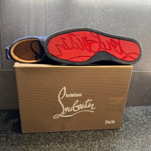 Blå mockasneakers från Christian Louboutin - Snygga sneakers från Christian Louboutin i mörkblå mocka med klassisk röd sula och diskret snörning. Skorna har rund tå och beige innersula, perfekt för dig som vill sticka ut med en lyxig touch. Boxen medföljer.