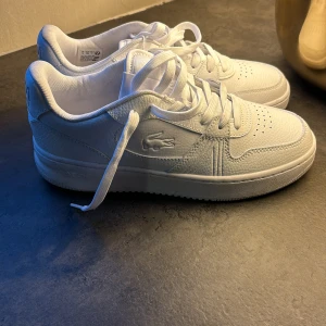 Vita sneakers från Lacoste i skinn - Säljer ett par fräscha vita Lacoste sneakers i skinn med klassisk krokodil-logga på sidan. Endast testade ett varv runt kvarteret. Strlk 38. Nyskick! 