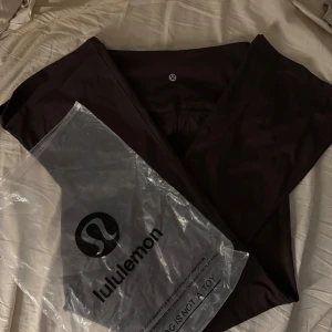 Bruna flare leggings från Lululemon - Mörkbruna leggings från Lululemon med hög midja och utsvängda ben. Tillverkade i ett stretchigt material av nylon och elastan som sitter riktigt snyggt. Perfekta för träning eller chill. Klassisk Lululemon-logga bak på linningen.