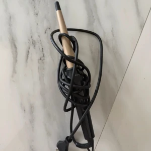 Locktång - Locktång med konisk design och svart handtag. Utrustad med lång sladd och EU-kontakt. Produkten ser ut att vara i gott skick utan synliga defekter eller slitage. Perfekt för att skapa vackra lockar snabbt och enkelt.