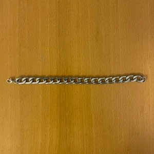 Kedjearmband i silverfärg - Stilrent kedjearmband i silverfärg med breda, platta länkar och karbinlås. Perfekt accessoar för dig som gillar en clean och modern look. Armbandet är robust och passar till många olika stilar.