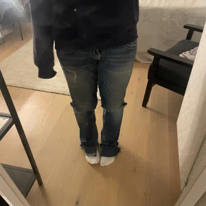 Mörkblå jeans med slitningar - Säljer ett par mörkblå jeans från True Religion med snygga slitningar och hål på benen. Modellen har raka ben, låg midja och coola detaljer som markerade sömmar och stora fickor med knappar bak. Perfekt för dig som gillar en avslappnad streetstil.