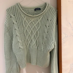 Ljusgrön stickad tröja från Dilvin - Snygg ljusgrön stickad tröja från Dilvin med grova flätstickade detaljer och ribbad kant. Tröjan har en rund halsringning och långärmade ärmar, perfekt för att hålla dig varm och stilren under kyliga dagar.