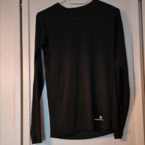 Svart långärmad funktionströja från Ronhill - En svart långärmad tröja från Ronhill med enkel och stilren design. Tröjan har rund halsringning och är tillverkad i polyester som passar perfekt för träning. Diskret logga nertill på framsidan.