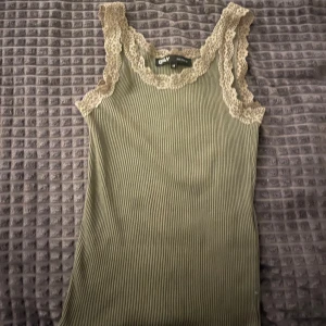 Olivgrön ribbad linnetopp från Only - Supersöt olivgrön ribbad linnetopp från Only med spetsdetaljer i beige runt halsringning och axelband. Toppen har en väldigt unik men ändå snygg look. Säljer då den inte kommer till användning längre. Skriv gärna om ni har några frågor 🥰💕