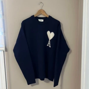 S men passar som M  - Snygg mörkblå stickad tröja från Ami Paris med ikoniskt vitt hjärta och A på bröstet. Tröjan har rund hals, ribbade muddar och en loose passform som ger en chill vibe. Perfekt för dig som gillar stilrena detaljer och vill sticka ut med en cool logga.