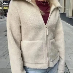 Beige teddyjacka med dragkedja - Säljer en beige teddyjacka med mjuk och fluffig yta. Jackan har två stora fickor framtill och stängs med dragkedja. Perfekt för dig som gillar en chill och cozy stil. I storlek s🥹