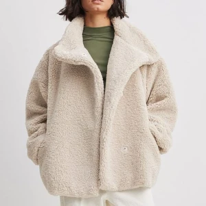 Beige teddyjacka med oversized passform - Supermjuk och fluffig teddyjacka i beige med stora slag och knappar framtill. Jackan har en oversized passform och är perfekt för kalla dagar. Tillverkad i syntetmaterial som ger en mysig känsla och cool look. Från NAKD, bra skick. Storlek 32 men den är oversized så skulle säga att den passar 32/34