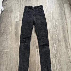 Svarta skinny jeans från Gina Tricot - Svarta jeans från Gina Tricot med skinny passform och hög midja. Byxorna har klassiska fem fickor, dragkedja och knapp framtill samt slits vid benslut. Tillverkade i bomull med en lätt tvättad look.