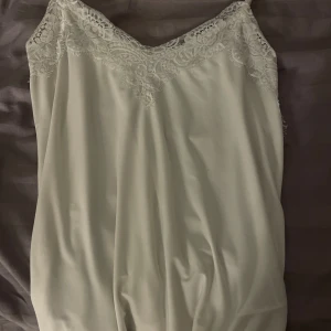 Vit spetslinne från Amisu  - Supersöt vit linne från Amisu i storlek XS. Linnet har tunna axelband och vacker spetsdetalj upptill både fram och bak. Materialet känns mjukt och har en lätt glans, perfekt för en fräsch look. Kan även användas som nattlinne om man vill. 