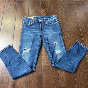 Blå jeans från Dondup - Snygga blå jeans från Dondup med slitna detaljer och hål på låren. Klassisk femficksmodell med orange sömmar och läderpatch bak i midjan. Jeansen har en smal passform och är tillverkade i stretchigt jeansmaterial för extra komfort.