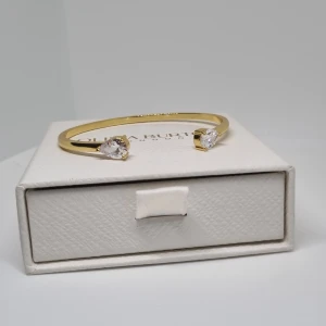 Guldarmband med droppformade stenar - Snyggt guldarmband med två droppformade, klara stenar i varje ände. Armbandet har en stilren och modern design som ger en lyxig känsla. Perfekt för dig som gillar eleganta detaljer och vill sticka ut med något glittrigt. Lådan ingår ej.