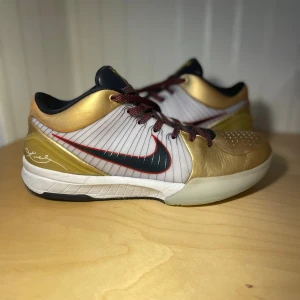 Nike Kobe 4 Protro Gold Medal  -  Använda några gånger. Nike Kobe 4 Protro Gold Medal sneakers med guld, vitt och svart i färgkombon. Skorna har röda snören, svart Swoosh med röd kant, och Kobe-logga på plösen. Ovandelen är i syntet och skinn, med perforeringar på tån och coola detaljer på sulan. 