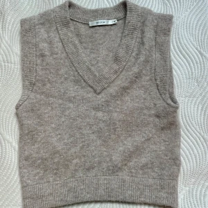 Beige stickad väst från Gestuz - Supersnygg beige stickad väst från Gestuz med v-ringad hals och breda ribbade kanter. 