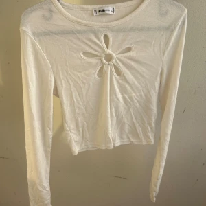 Vit långärmad topp med blomdetalj - Supersöt vit långärmad topp med en blomformad cut-out framtill. En längre Croppad passform och rund halsringning. Den va väldigt liten i storleken så den är L men mer som M. Jag har S/m och den är mkt förliten för mig vid armarna. Den är lite genomskinlig (som man kan se vid galjen som är svart). (Ganska tunt tyg)✨och mycket stretch i✨