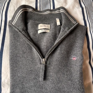 Grå half zip tröja från GANT - Snygg grå långärmad tröja från GANT med half zip och ribbad krage med vita ränder. Tröjan är i mjuk lammull.   Helt oanvänd half zip ifrån gant, jätte fin. Storlek L.     Ny pris 1 700 Pris kan diskuteras 