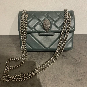 Grön väska från Kurt Geiger - Snygg äkta quiltad axelväska från Kurt Geiger i mörkgrönt skinn med silverfärgad kedja. Väldigt bra skick och inga defekter.