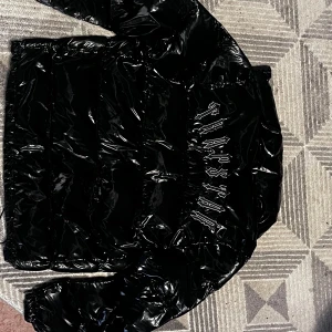 Trapstar Puffer Jacka - Säljer en svart glansig pufferjacka från Trapstar med fet logga i vitt på ryggen. Jackan har dragkedja, knappdetaljer och snörning nedtill. Perfekt för dig som vill sticka ut med streetstyle och hålla dig varm under kalla dagar.