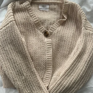 Beige stickad kofta från Zara - Säljer en beige stickad kofta från Zara med v-ringning och en stor knapp framtill. Koftan har långärmade ärmar och grovstickad struktur som ger en chill och mysig vibe. Är i stolek 165 men är overaize så passar xs-s