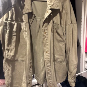 Grön jeansjacka Zara  - Snygg grön overshirt med stora bröstfickor och knappar framtill. Skjortan har en avslappnad passform och är tillverkad i mjuk bomull, perfekt att slänga över en t-shirt. Långärmad och med klassisk krage för en chill look.