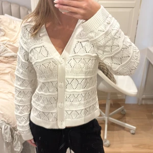 Vit stickad kofta från Object XS - Säljer en vit stickad kofta från Object i storlek XS. Koftan har ett hålmönster med diamantformade detaljer, v-ringad hals och stora knappar framtill. Långärmad och ribbade muddar vid ärmslut och nederkant. 
