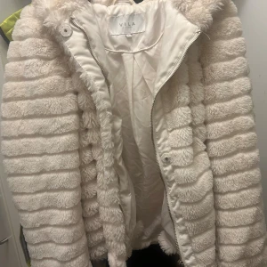 Vit pälsjacka från VILA - Säljer en fluffig och mysig vit pälsjacka från VILA med  ränder och dragkedja framtill. 